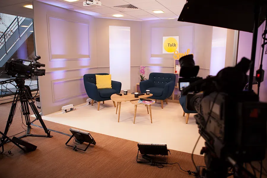 Plateau de talk show chaleureux, fauteuils bleus et lumière douce, caméras au premier plan